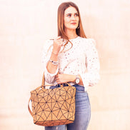 Woman holding a geometric-patterned tan bag against a plain background
