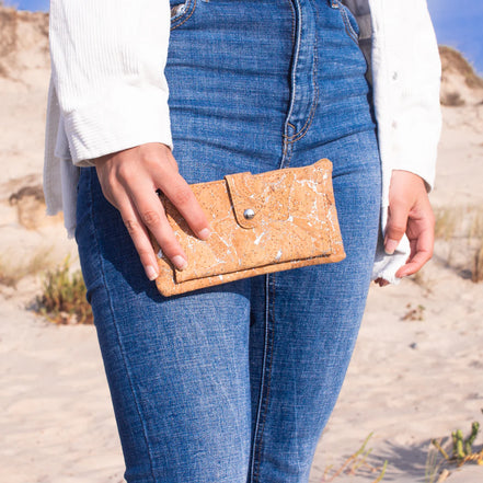 Hand holding metallic cork wallet on beach background