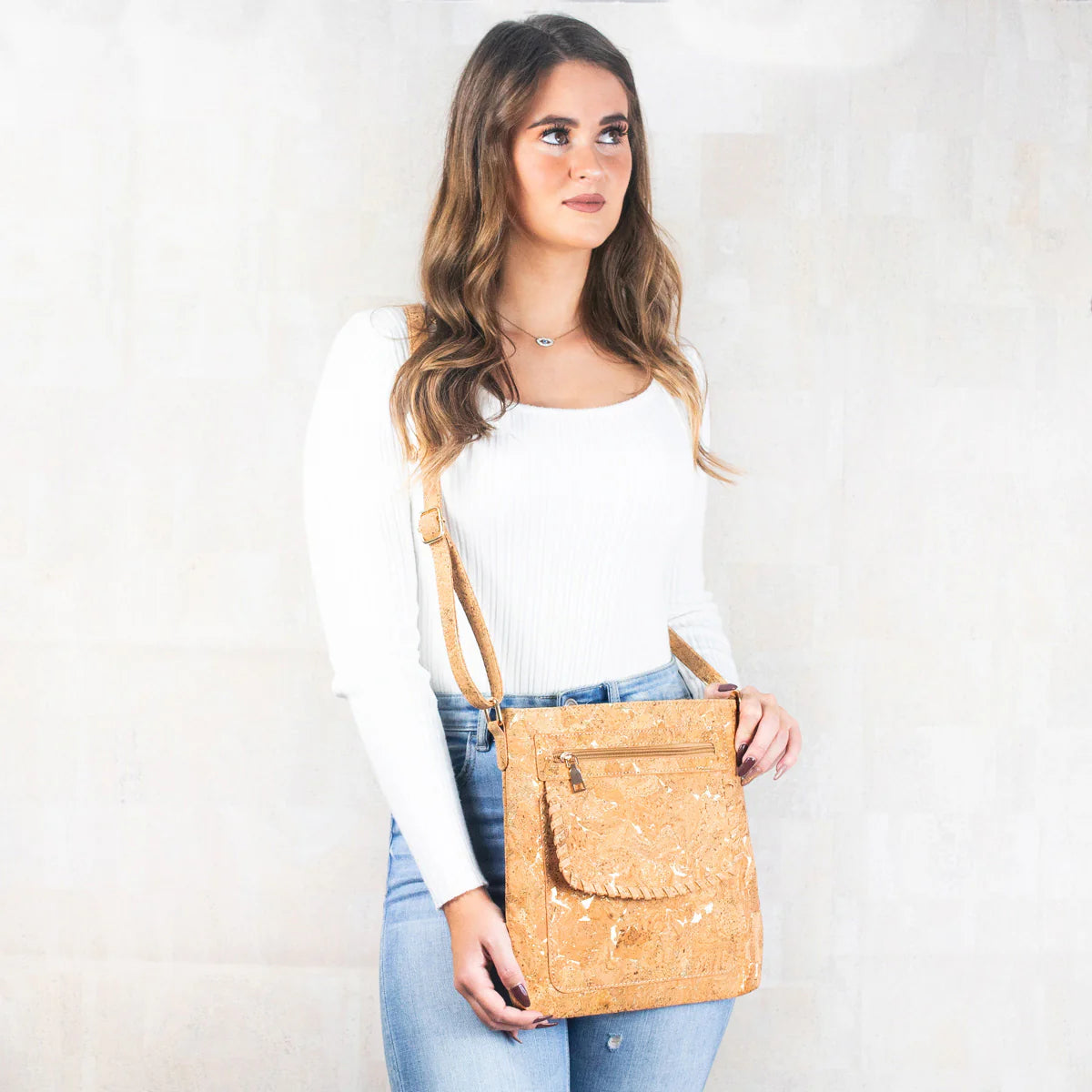 Woman holding a tan crossbody bag against a white background