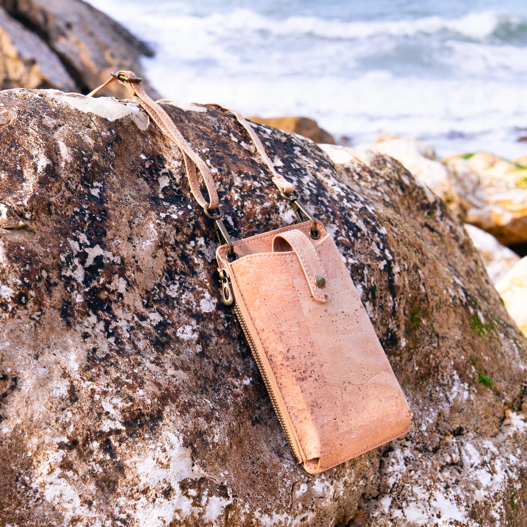 Lifestyle photo of natural cork phone pouch on rocks near ocean